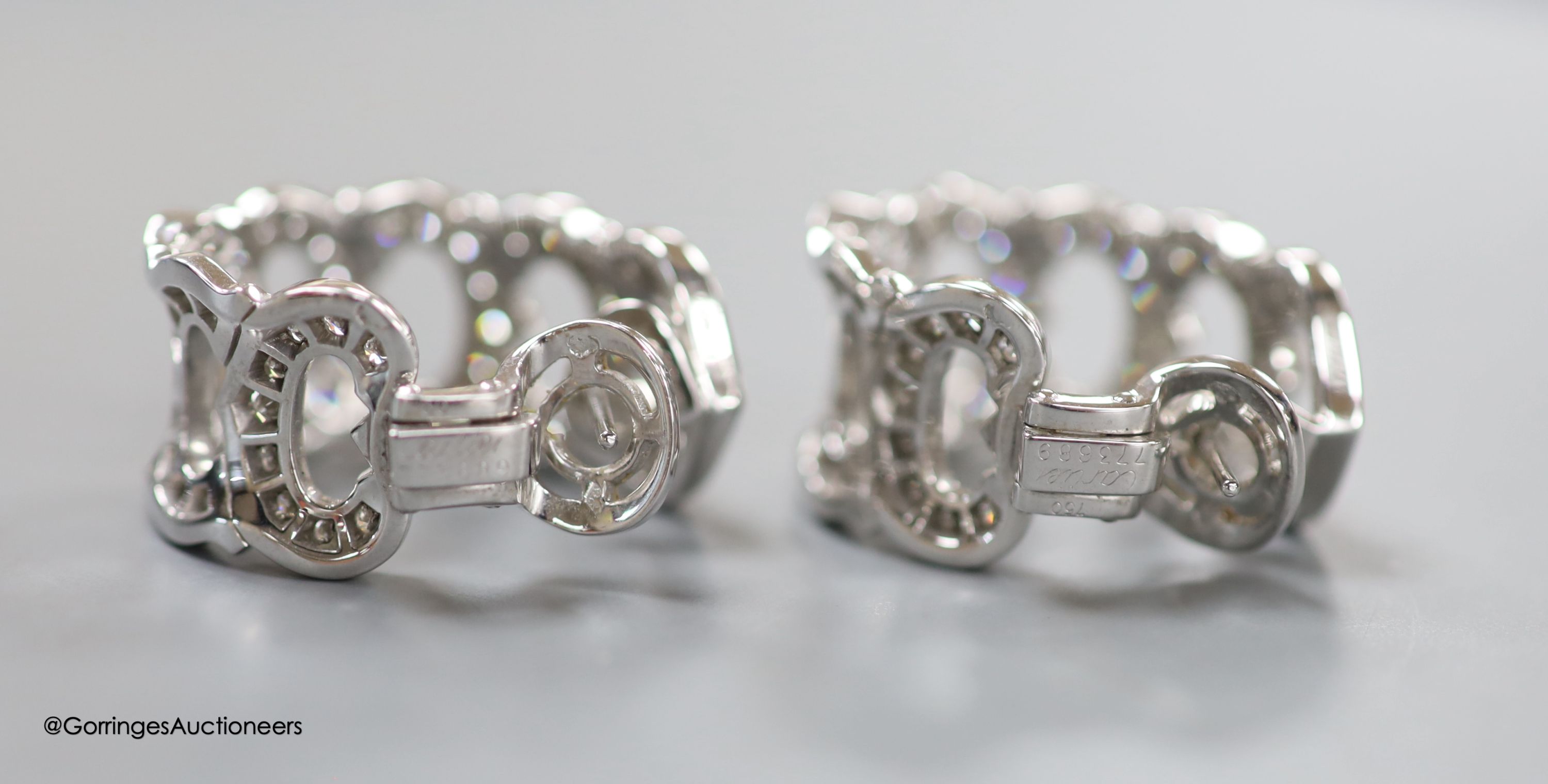 A modern pair of French Cartier white metal (18ct poincon mark) and diamond encrusted '7 C's' earrings, of curved form